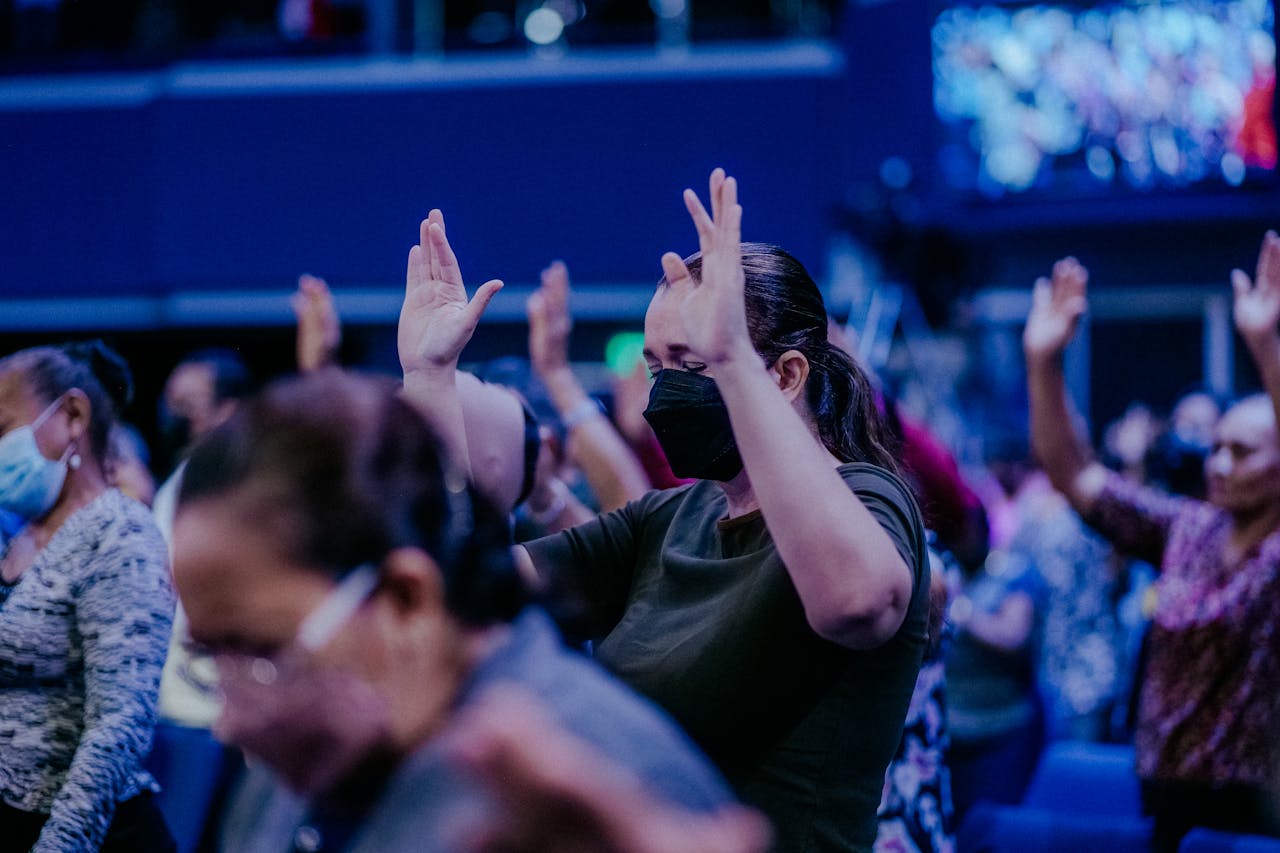 digital-01 Women worship indoors with raised hands and face masks, capturing vibrant religious fervor.